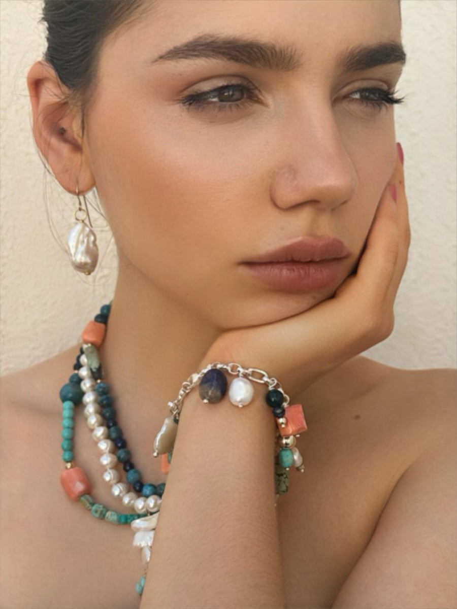 Dark haired girl wearing Leoni & Vonk jewellery. Her chin is in her hands and she is looking to the side of the image.