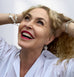 Blonde curly haired woman laughing and looking up. She has her hair in her hands and is wearing Leoni & vonk jewellery