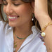 Dark haired girl smiling with her hands in her hair. She is wearing Leoni & Vonk jewellery and a white shirt.
