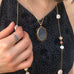 Cropped image of a woman wearing a blue dress and Leoni & Vonk jewellery. She is holding a necklace which is round her neck
