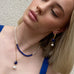 Blonde model wearing Leoni & Vonk September sapphire and lapis  jewellery. She is leaning back against a white wall and has her chin up.
