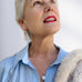 Woman with grey hair wearing a blue shirt and leoni & Vonk pearl jewellery. She is looking up to the right of the image and has a cream fur coat on her shoulder.