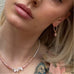 Blonde girl with her head tilted wearing Leoni & Vonk pink opal jewellery and a floral top.