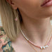 Blonde girl wearing Leoni 7 Vonk pink opal jewellry and a floral top. The image is cropped to show her neck and chin.