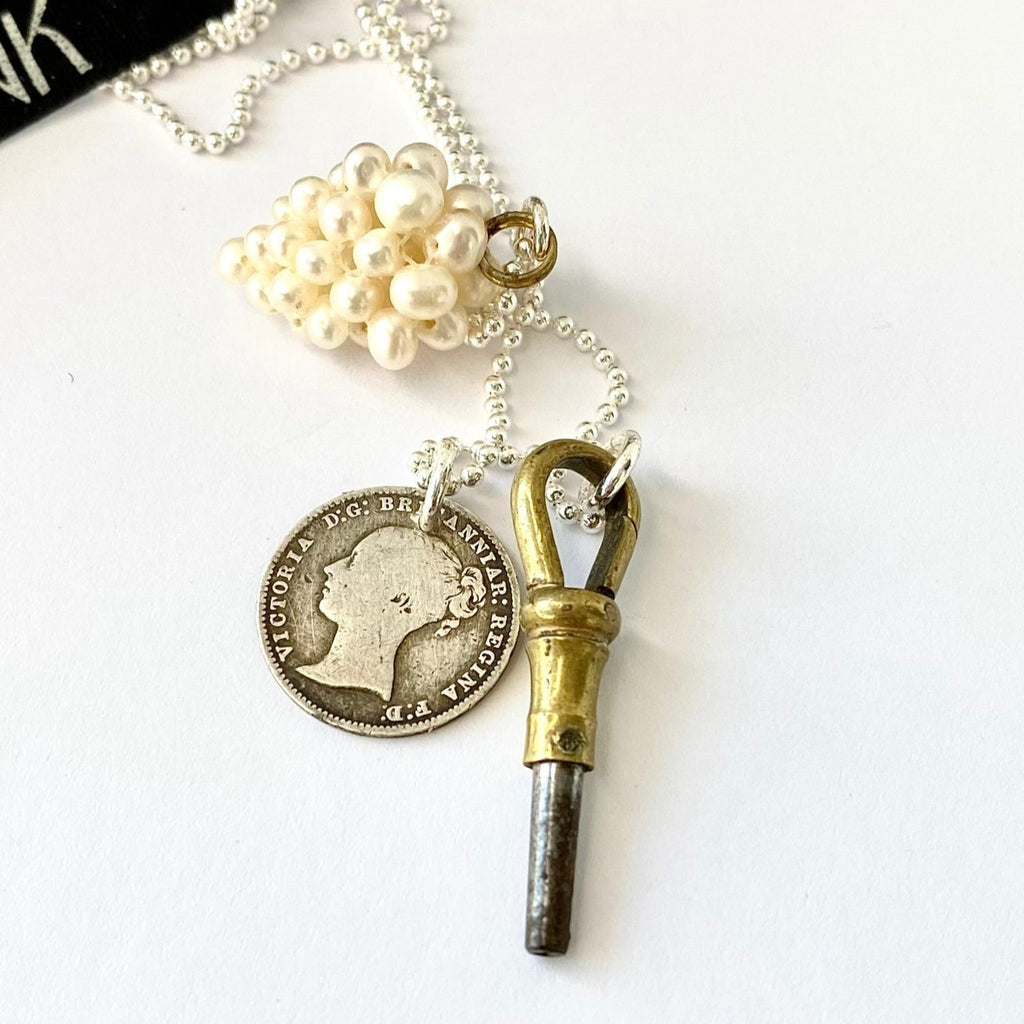 Leoni & Vonk antique watch key and 1868 threepence charm neckalce on a white background with Leoni & Vonk ribbon