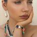 Dark haired model with her chin in her hands. She is wearing Leoni  & Vonk multi  gemstone and pearl jewellery.