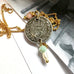 Leoni & Vonk antique 1906 threepence necklace on a gold chain on a white background and with a vintage postcard