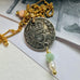 Leoni & Vonk antique 1906 threepence necklace on a gold chain on a white background and with a vintage postcard