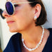 Dark haired woman wearing a dark blue top and Leoni & Vonk pearl jewellery and blue round sunglasses