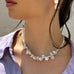 Cropped image of a dark haired girl wearing white sunglasses and Leoni & Vonk jewellery. She is also wearing a lilac shirt and is looking to the left of the image
