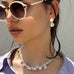 Dark haired girl wearing white sunglasses and Leoni & Vonk jewellery. She is also wearing a lilac shirt and is looking to the left of the image