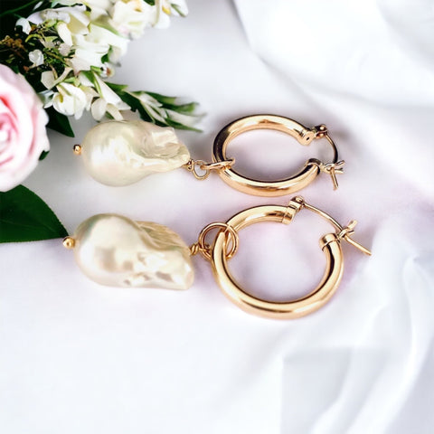 Leoni & Vonk baroque pearl and gold hoop bridal earrings on a white fabric background and bridal flowers