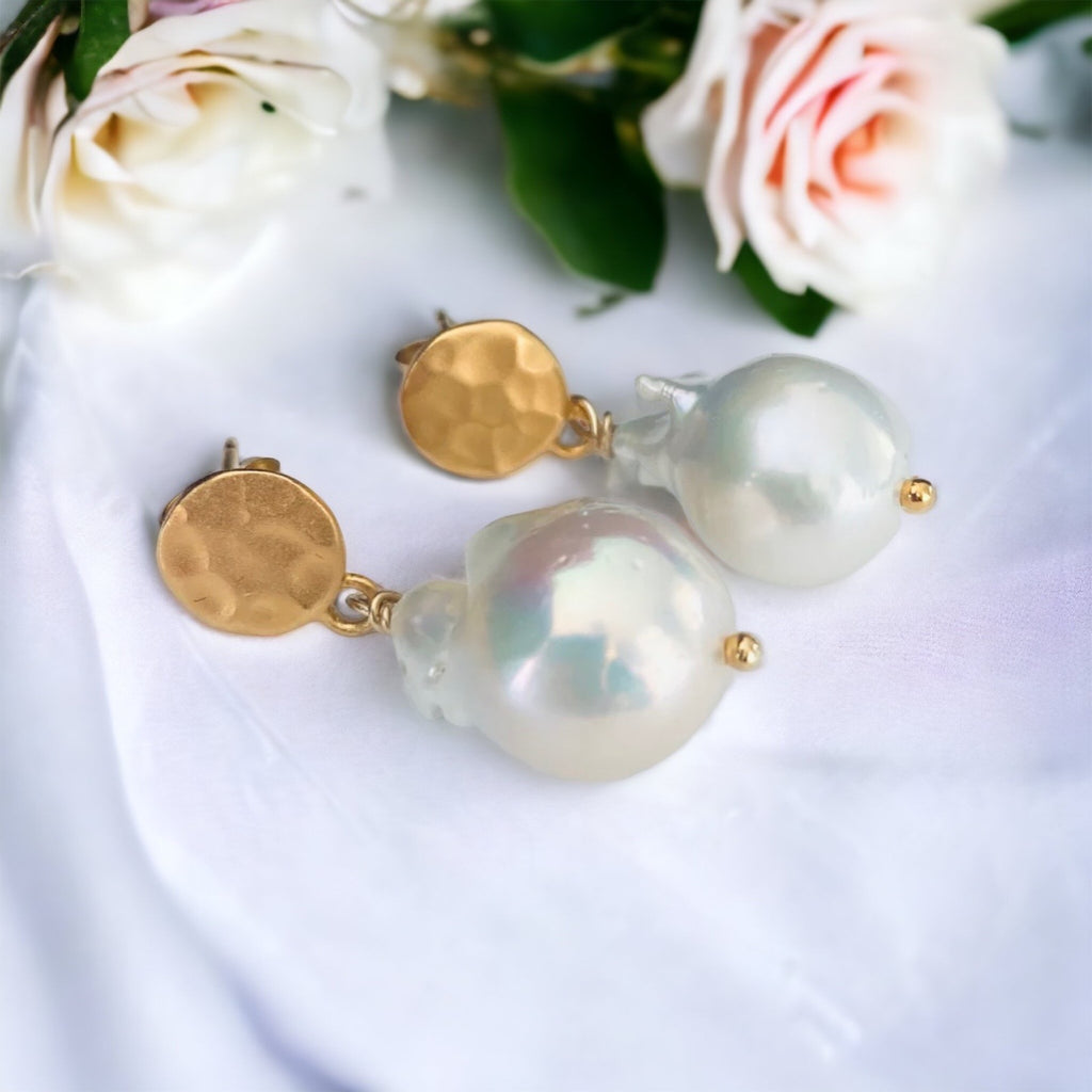 Leoni & Vonk baroque pearl gold stud earrings on a white fabric background and bridal flowers.