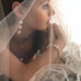 Dark haired bride wearing Leoni & Vonk pearl jewellery and a veil. She is looking out to the right of the image.
