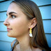 Girl standing against a blue wall and wearing Leoni & Vonk cascading gold pearl earrings