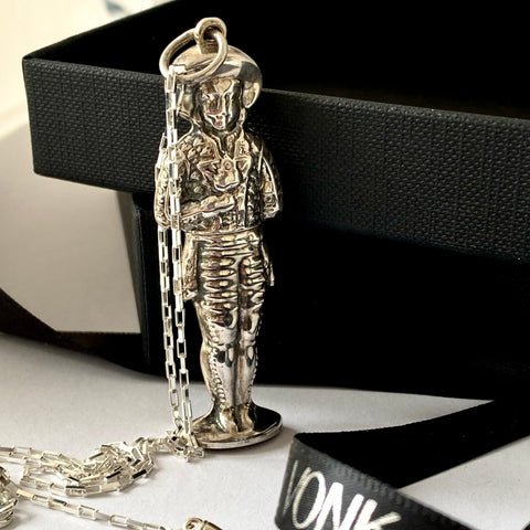 Leoni & Vonk vintage silver needle case necklace on a white surface next to a black box. The needle case is in the shape of a man holding a bunch of flowers.