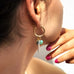 Cropped image of a girls neck and ears. She is wearing Leoni & Vonk gold hoop charm earrings and you can see her hand in the background