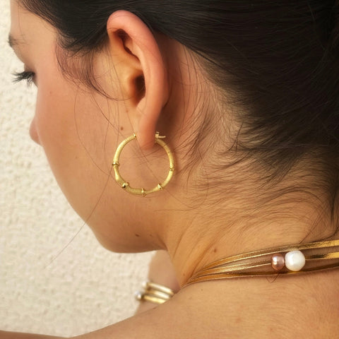 Image of the back of the neck of a dark haired girl. She is wearing Leoni 7 Vonk gold hoop earrings and a leather and pearl necklace.