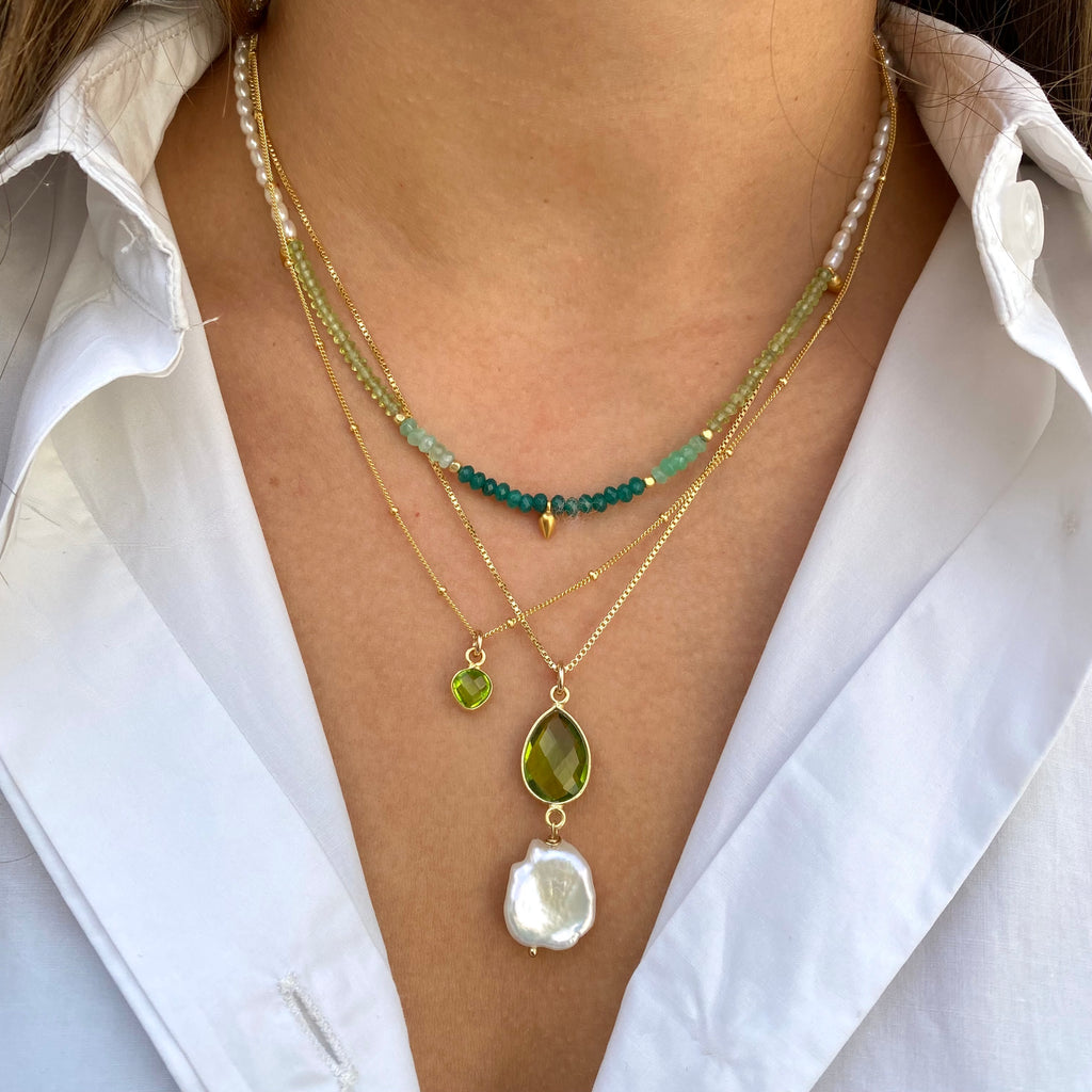 Image of a girls neck wearing Leoni & Vonk peridot and pearl necklaces and a white shirt