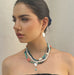 Dark haired model looking to the side of the image wearing Leoni & Vonk necklaces and pearl earrings