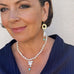 Dark haired woman wearing a blue pleated top looking out of the camera. She is wearing Leoni & Vonk pearl jewellery