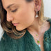 Image of a girls neck and hair. She is wearing Leoni  & Vonk peridot  August peridot birthstone jewellery and silver charm pearl earrings and a green fur jacket
