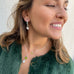 Dark haired girl smiling and looking to the side of the image. She is wearing Leoni & Vonk August peridot Leoni & Vonk jewellery and a green jacket.
