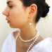 Dark haired girl wearing a white shirt and leoni & Vonk pearl jewellery. She is looking out to the side of the camera