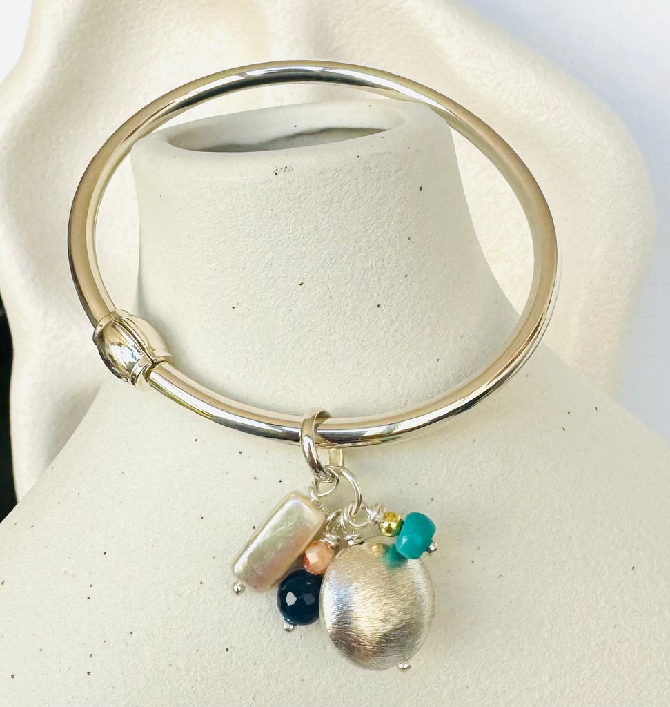 Leoni & Vonk sterling silver bangle with sterling silver and pearl charms on a white vase