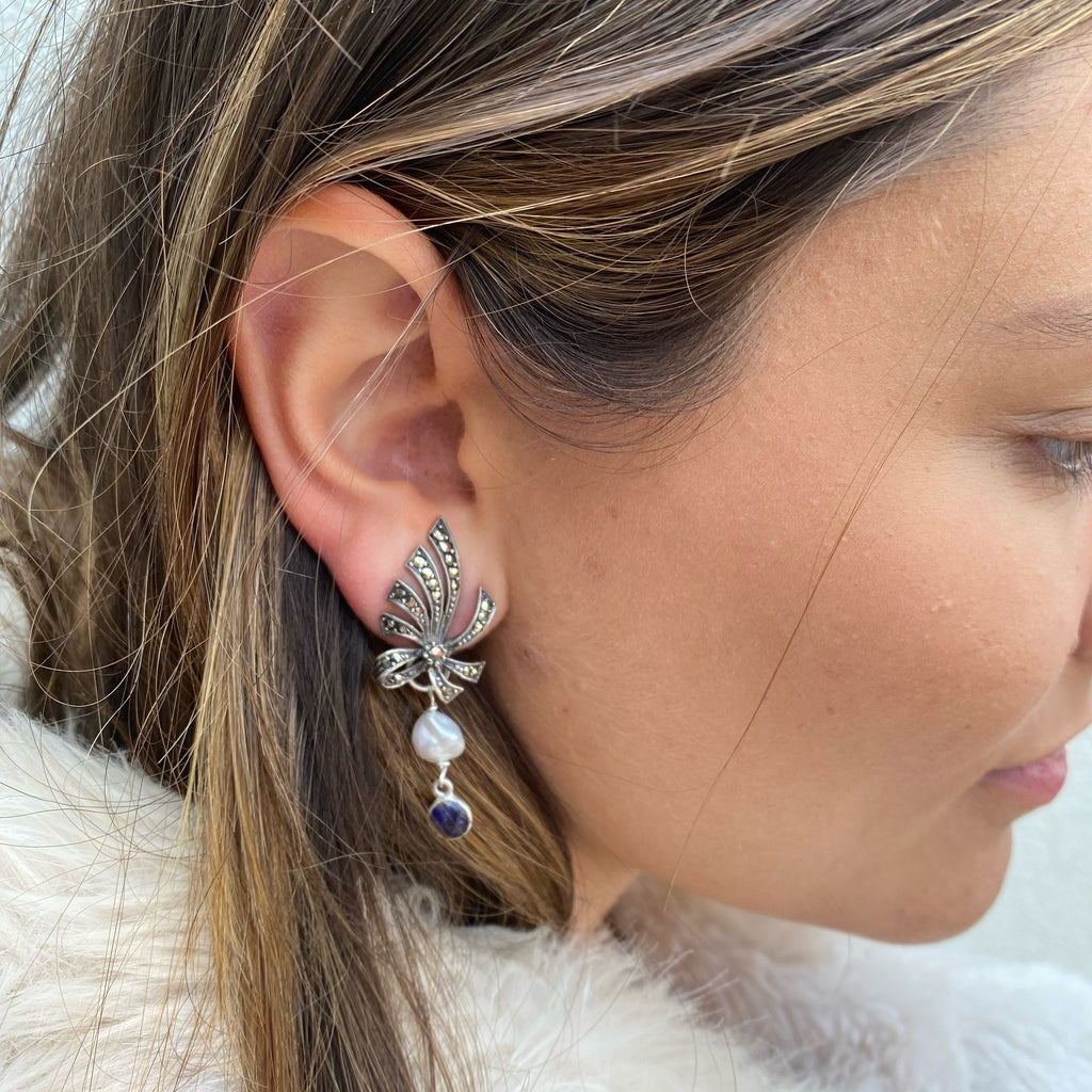 Dark haired girl wearing marcasite and pearl and sapphire earrings and a cream fur coat.