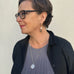 Cropped image of a woman wearing a Leoni & Vonk vintage stokes medallion necklace and a grey dress and black jacket