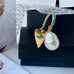 Leoni & Vonk pearl and gold heart earrings on a black box with white flower ribbon