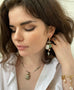 Dark haired model holding her hair behind her ear wearing Leoni & Vonk jewellery and a white shirt. She is looking down to the left of the image.