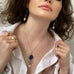 Dark haired girl wearing a white shirt and A Leoni & Vonk lapis, coin and pearl necklace. She is holding the collar of the shirt to show the necklace and you can only see her mouth as the image is cropped.