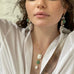 Dark haired model holding her hands behindher head and wearing a white shirt and Leoni & Vonk pearl and aqua chalcedony jewellery. Her eyes are slightly closed.