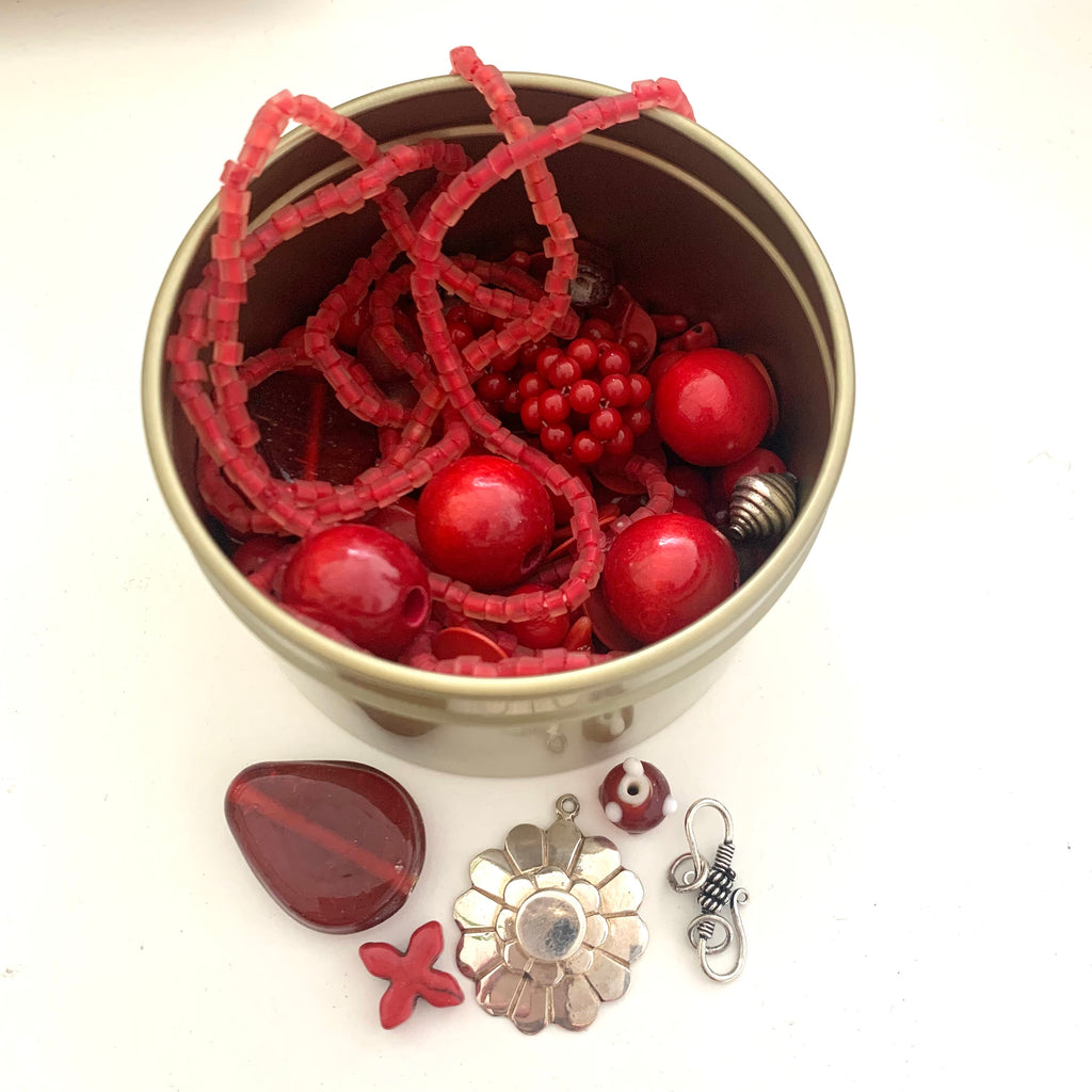 Leoni & Vonk bead tin containing red beads of all different shapes and sizes. 