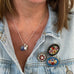 woman wearing a denim jacket with sapphire and pearl charm necklace and vintage micro mosaic brooches