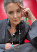 Modle with grey hair wearing Leoni & Vonk jewellery standing against a red wall.